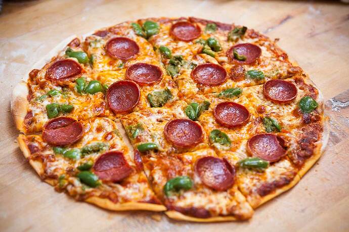 St-Louis-style-pizza cut into 2-inch squares: very flat unleavened crust with lightly-browned Provel cheese, pepperoni crisped to a cup-shape, and green basil leaves.